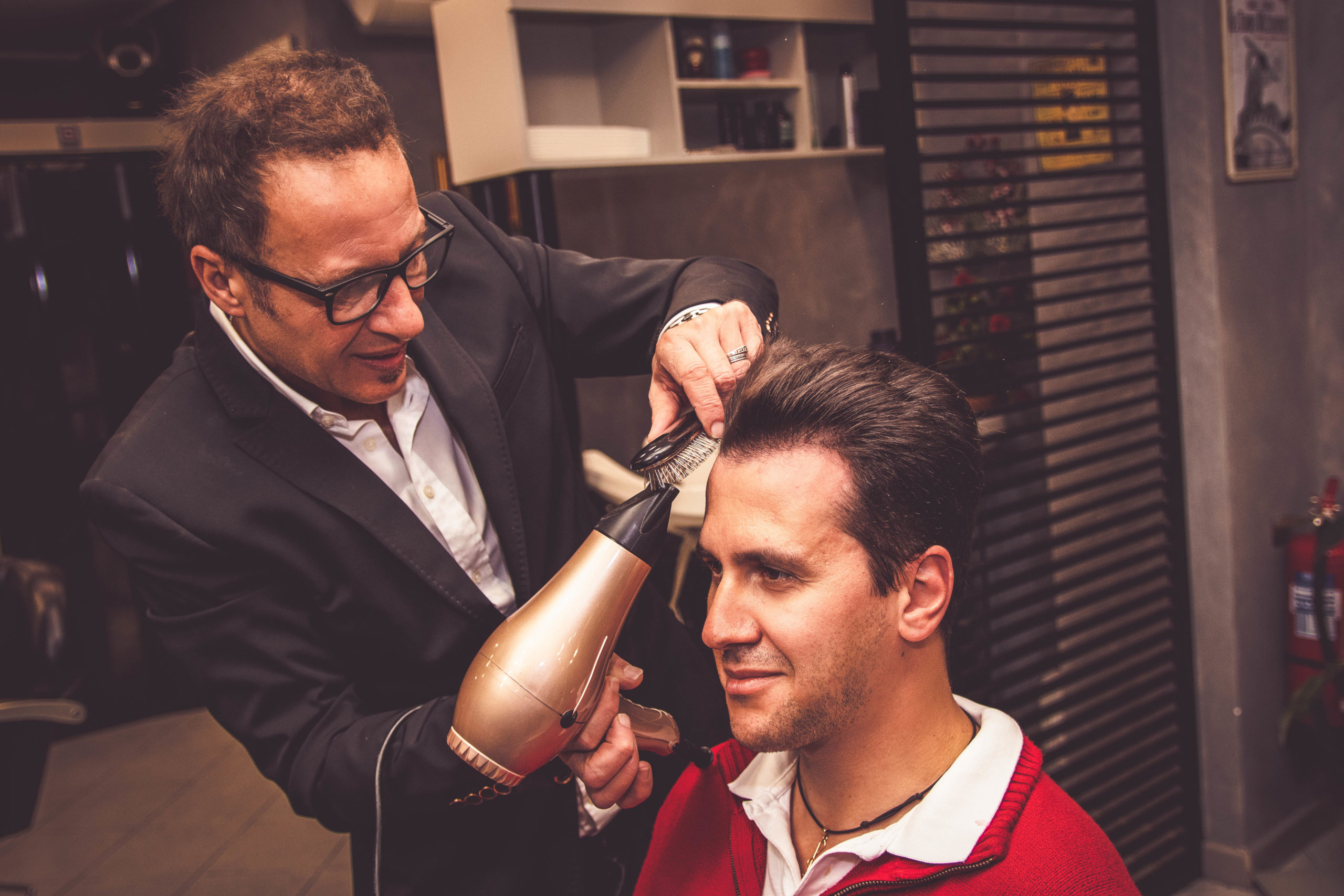 Barbiere professionista che modella i capelli di un cliente con phon e spazzola da Parrucchiere Uomo Orlando a Cologno Monzese.